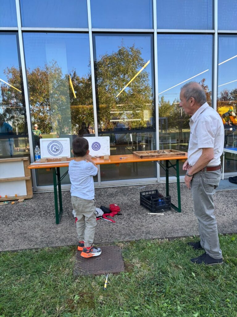 Un bambino prova un gioco di mira con bersagli disegnati, mentre un adulto lo osserva